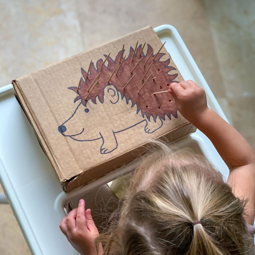 child playing game to strengthen fine motor skills by poking toothpicks or cotton swabs into a box shaped like a porcupine