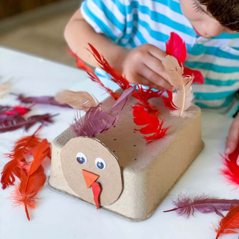 A toddler poking paper feathers into a turkey craft