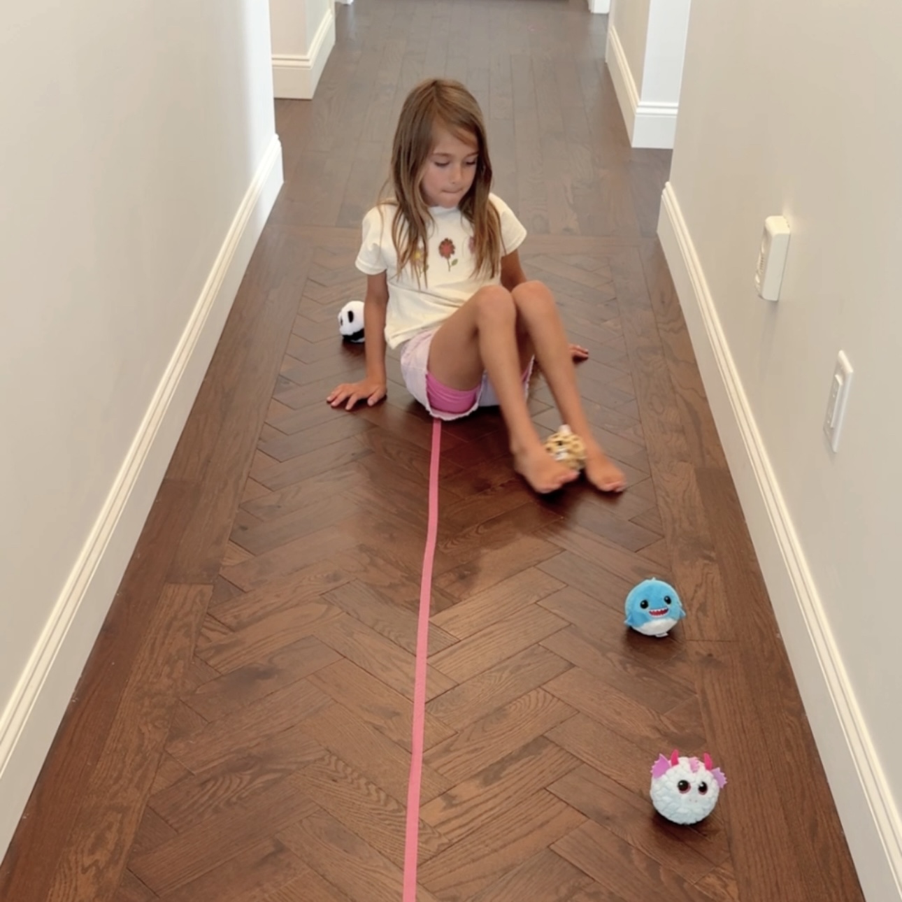 Child sitting and using feet to pass plush balls over a pink tape line on the floor