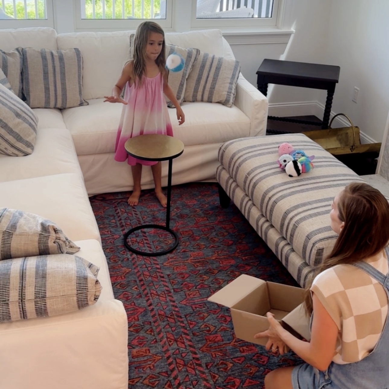 Child bouncing a plush ball off a table while an adult catches it in a cardboard box