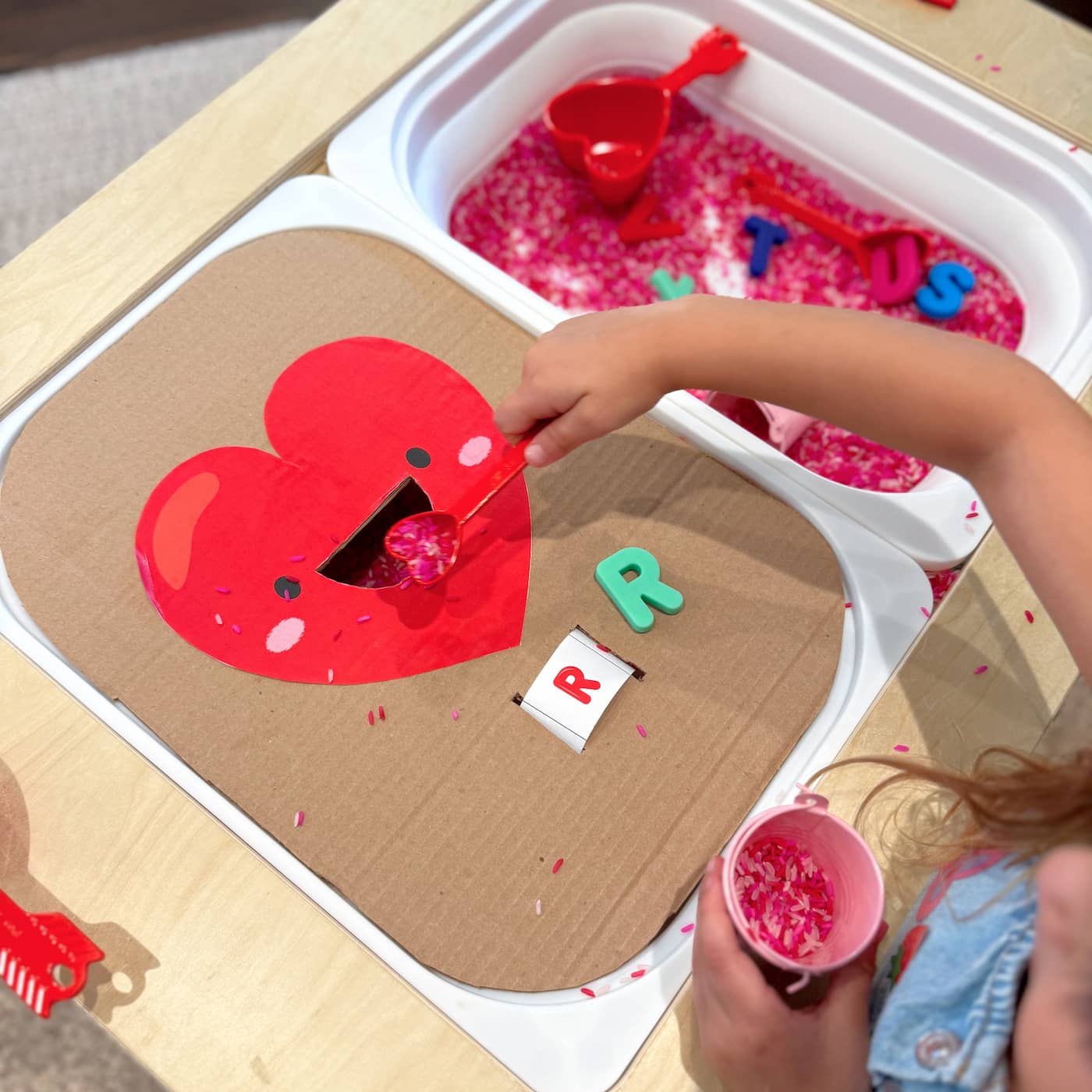 Valentine’s Sensory Rice Play Station — Overhead View Overhead view of a Valentine’s sensory rice activity on a foldable kids sensory table with pink rice, scoops, cups, and a cardboard heart letter feeder.