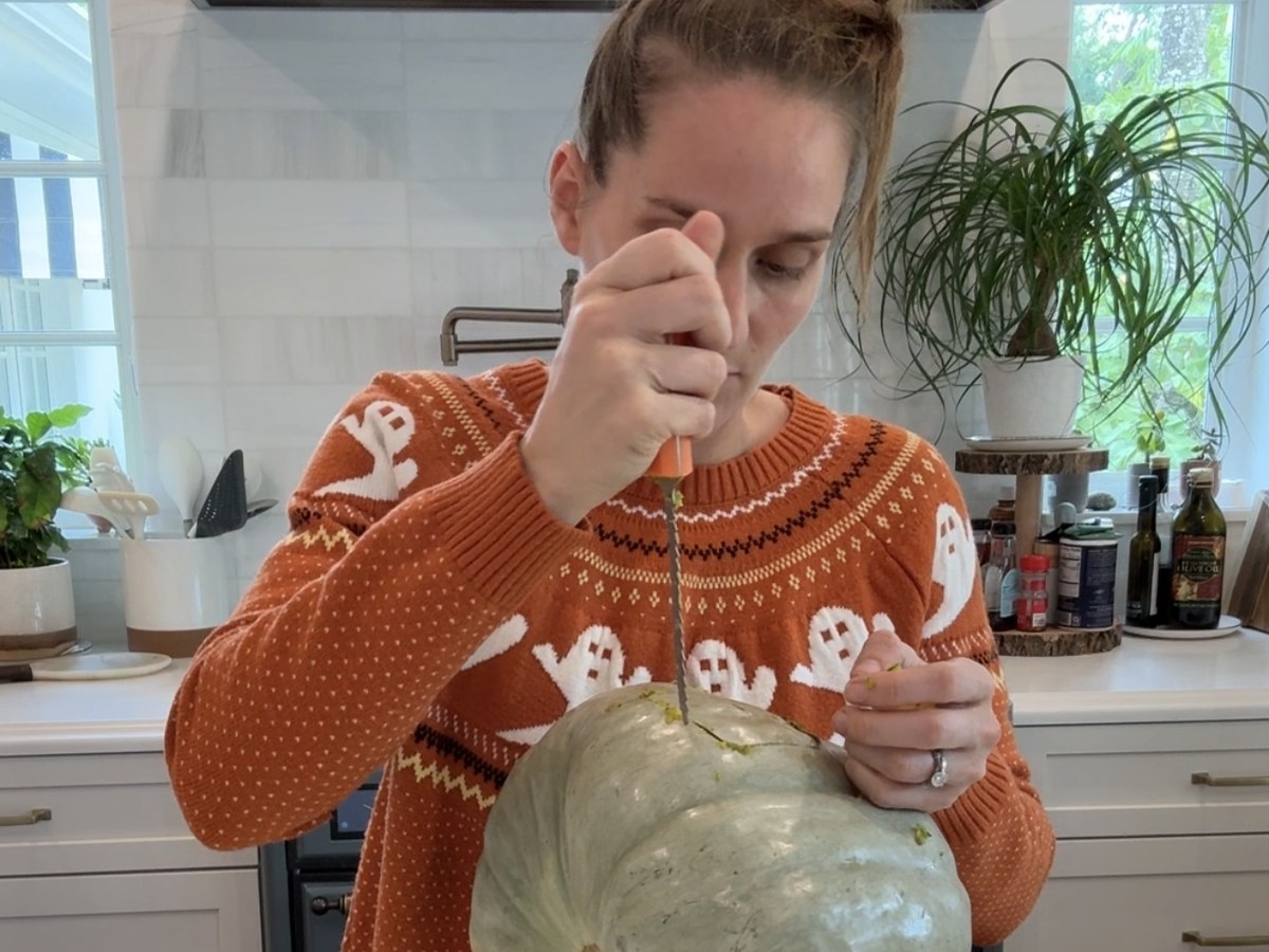 Cutting a small door into a pale green pumpkin with a serrated pumpkin saw