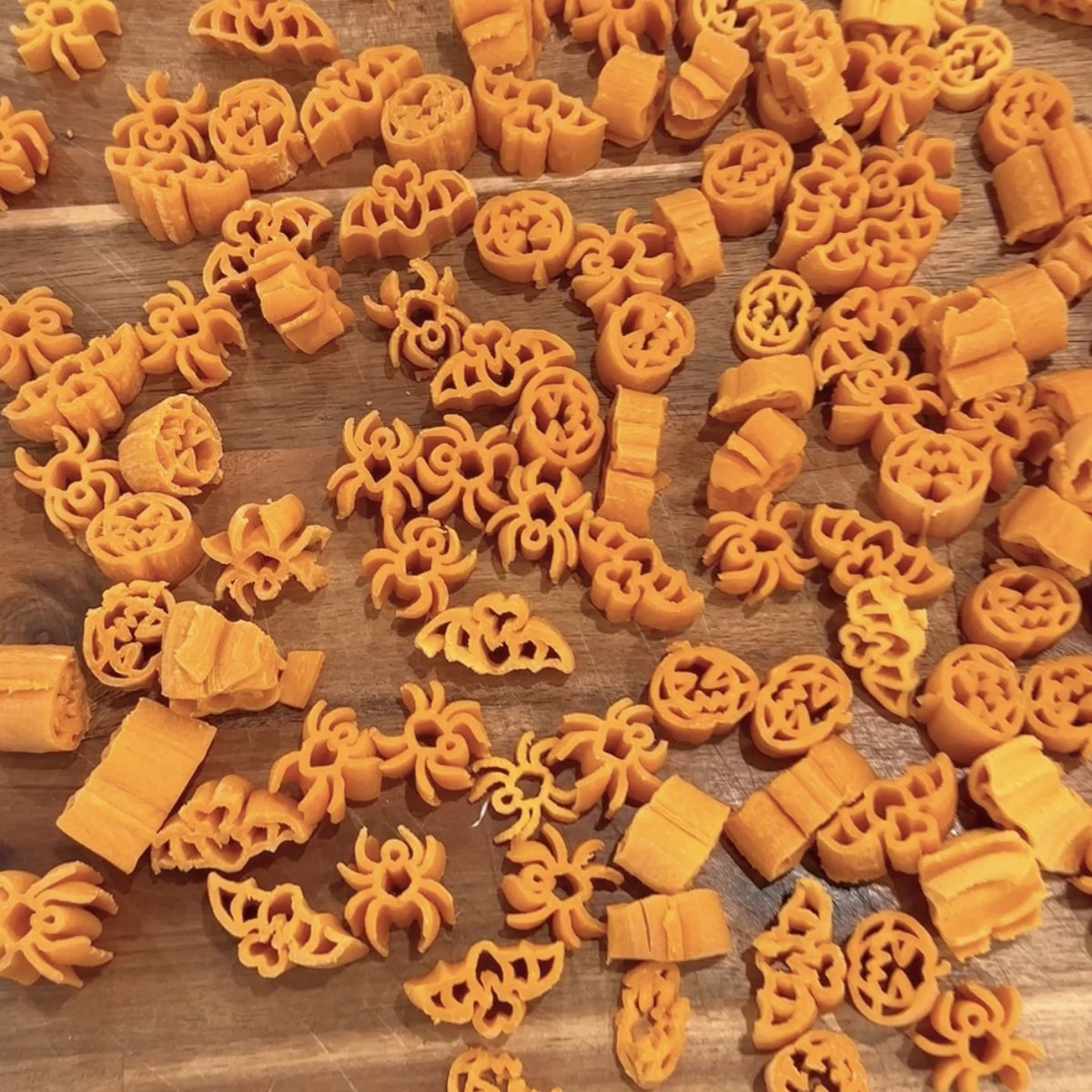 Orange Halloween pasta shapes made with Philips pasta maker discs, including pumpkins, bats and spiders, on a wooden board